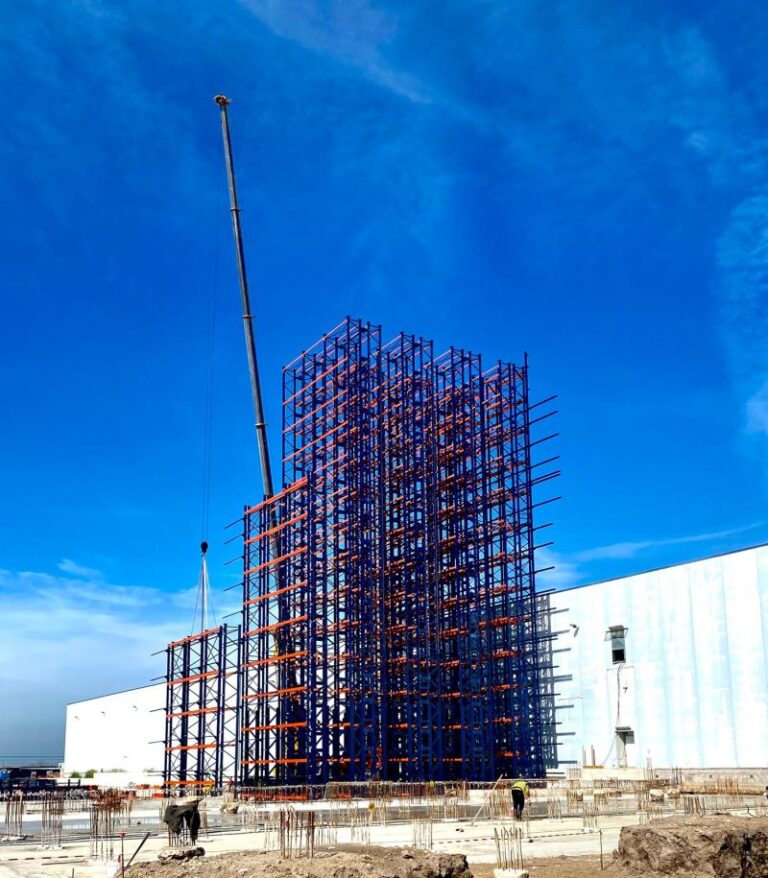 Montaggio di una struttura metallica in un cantiere industriale con una gru di sollevamento.